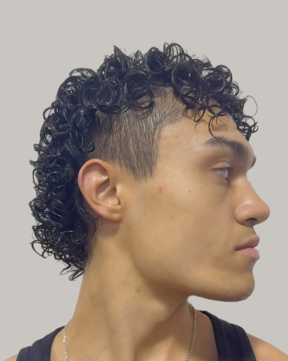 Man with a tightly curled mullet and short sides, seen in profile