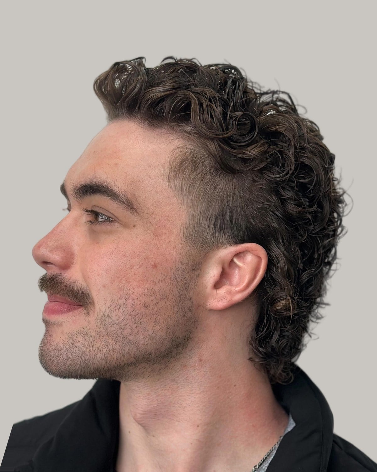 Man with a mustache and a curly permed mullet, seen in profile
