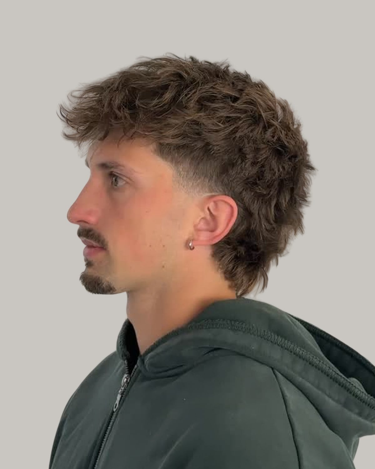 Man with a short brown curly mullet and a mustache, seen in profile