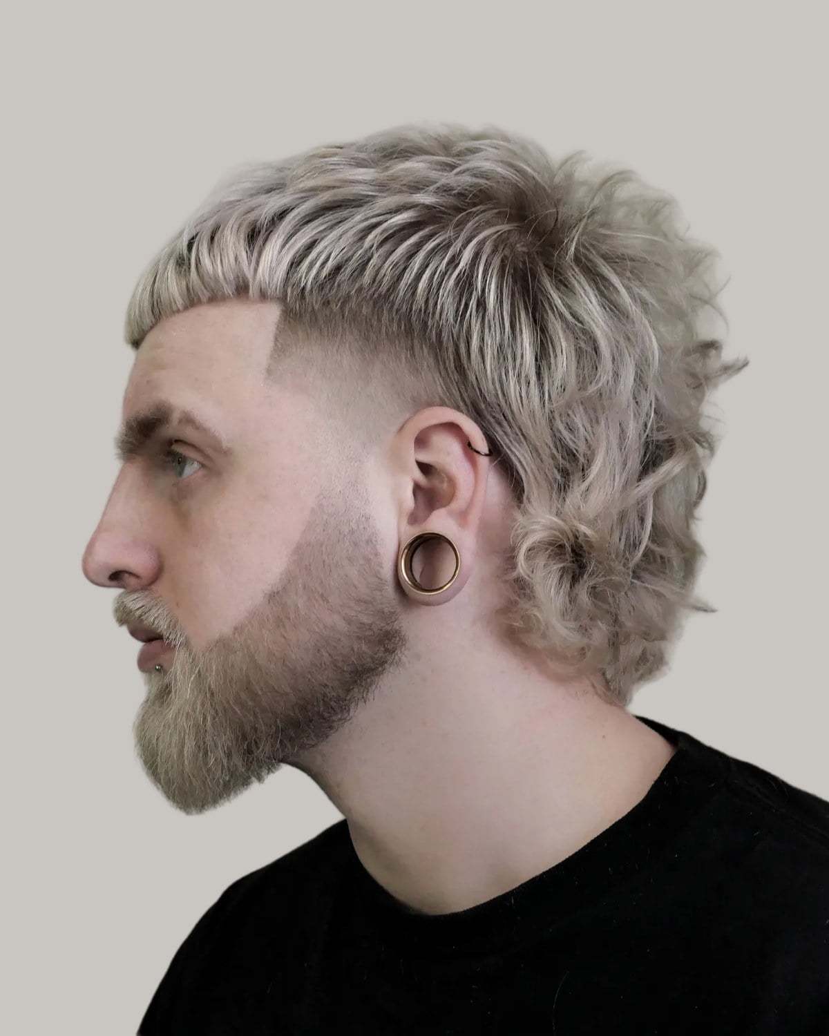 Bearded man with a short platinum blond mullet, wavy at the back, and a skin fade, seen in profile