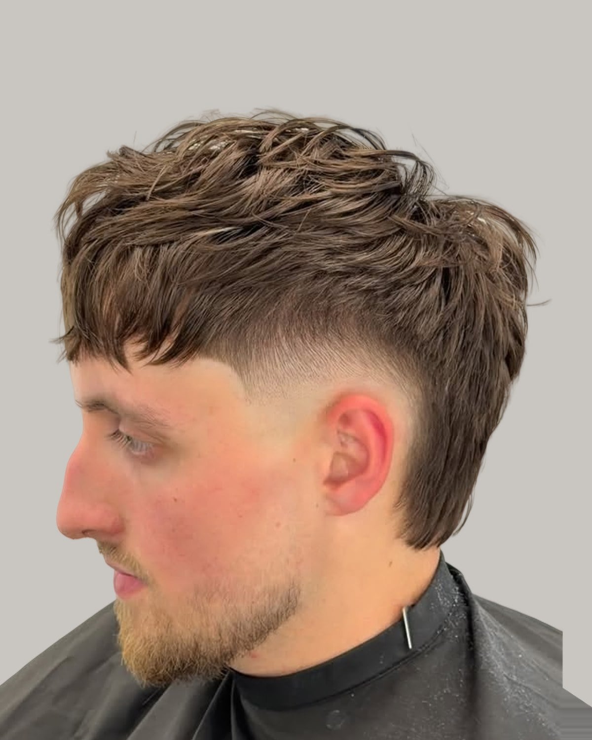 Man with a brown textured mullet, a heavy fringe and a skin fade, seen at an angle