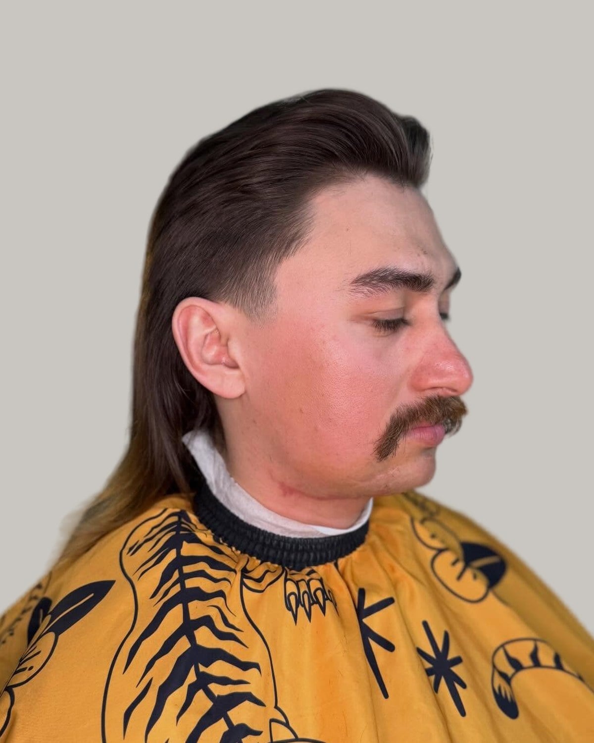 Man with a mustache and a slicked-back mullet, looking down at an angle