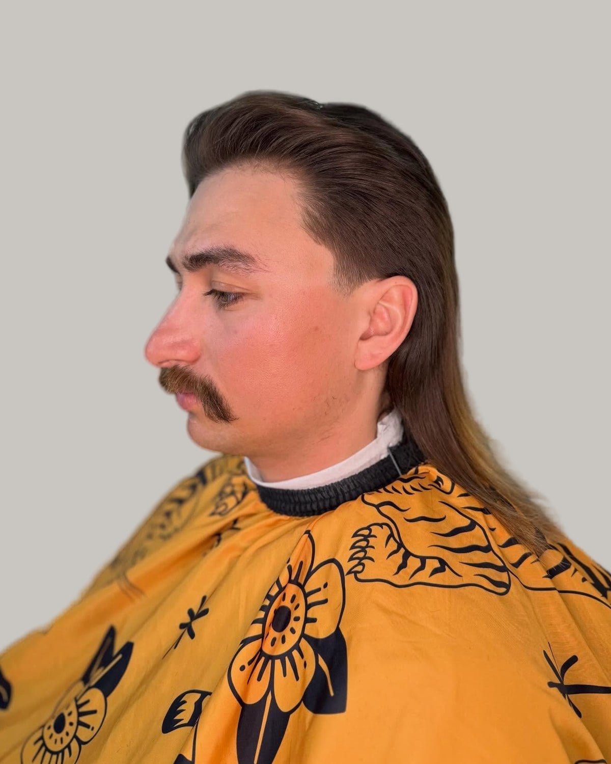 Man with a mustache and a long slicked-back mullet, seen in profile