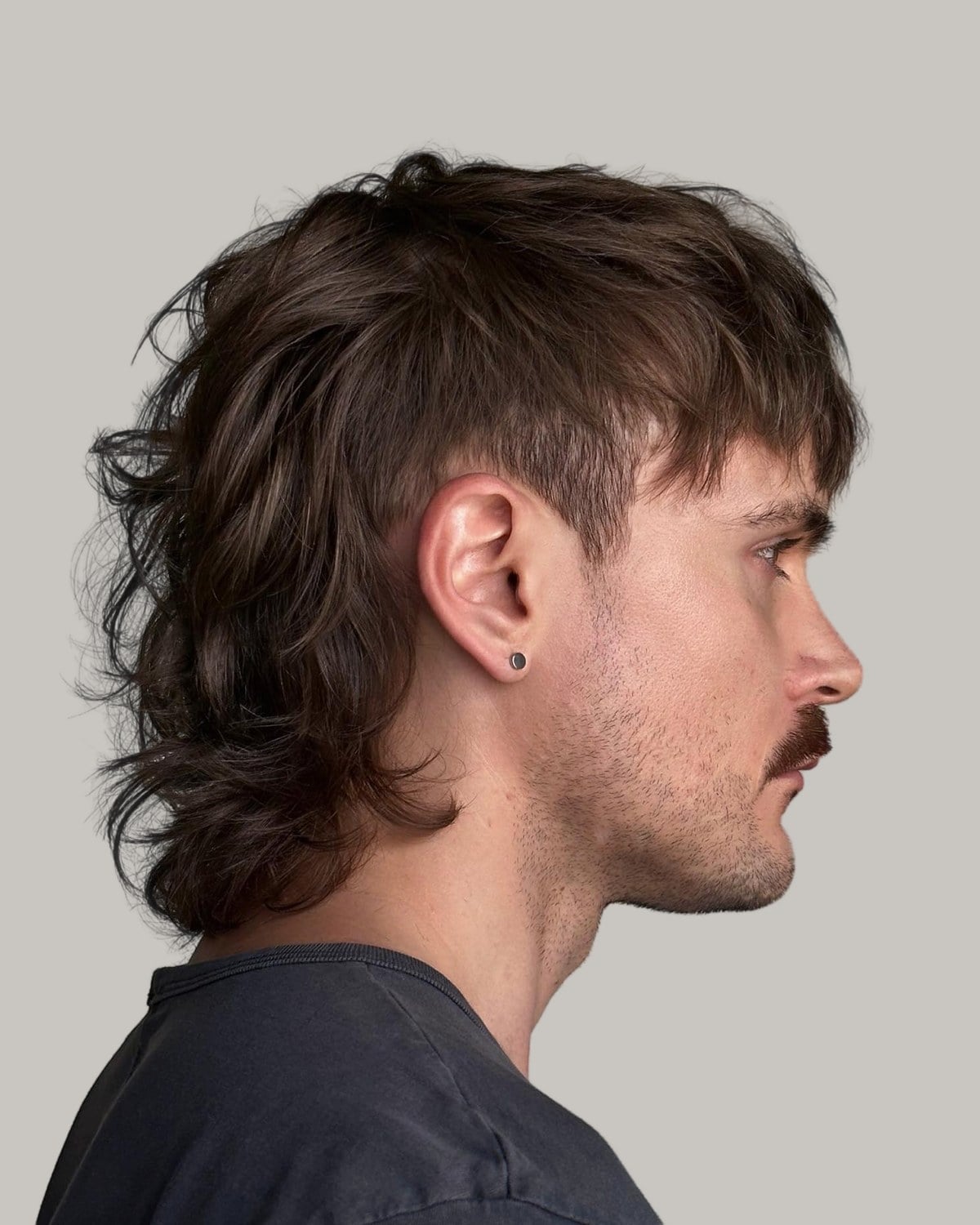 Man with a mustache and a layered brown mullet with a temple taper, seen in profile