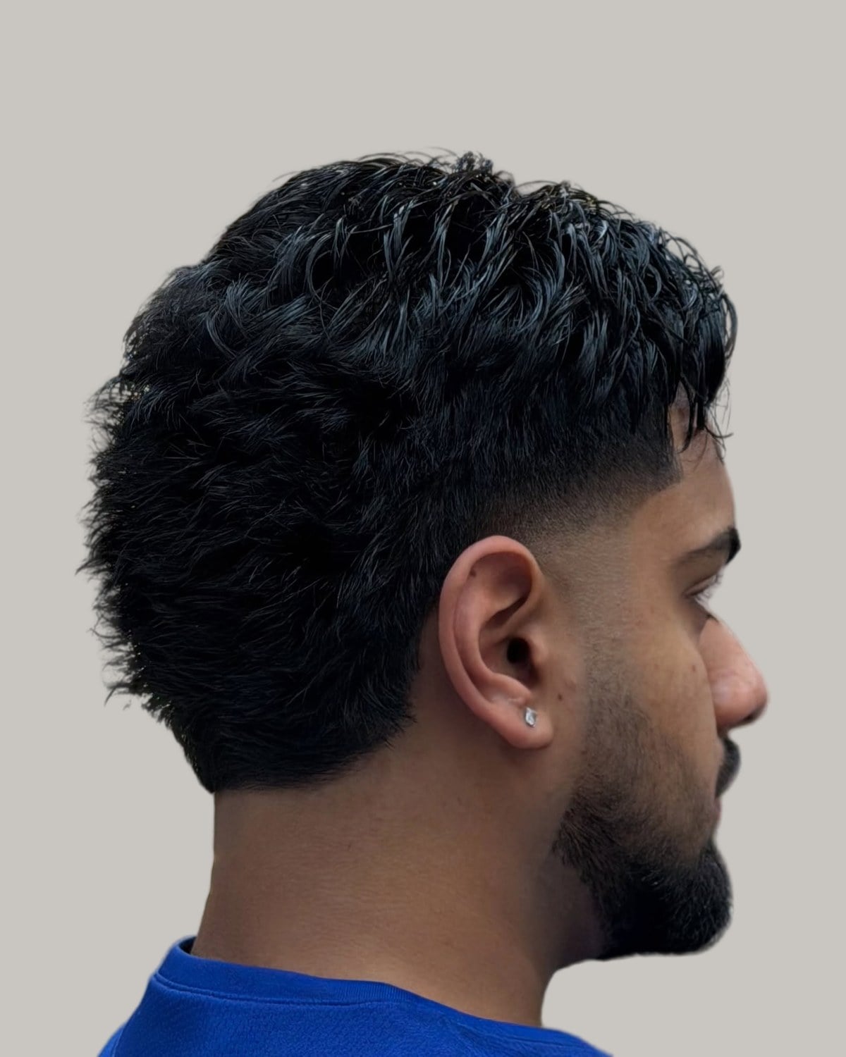 Bearded man with a dense, textured black mullet and a fade, seen from behind at an angle