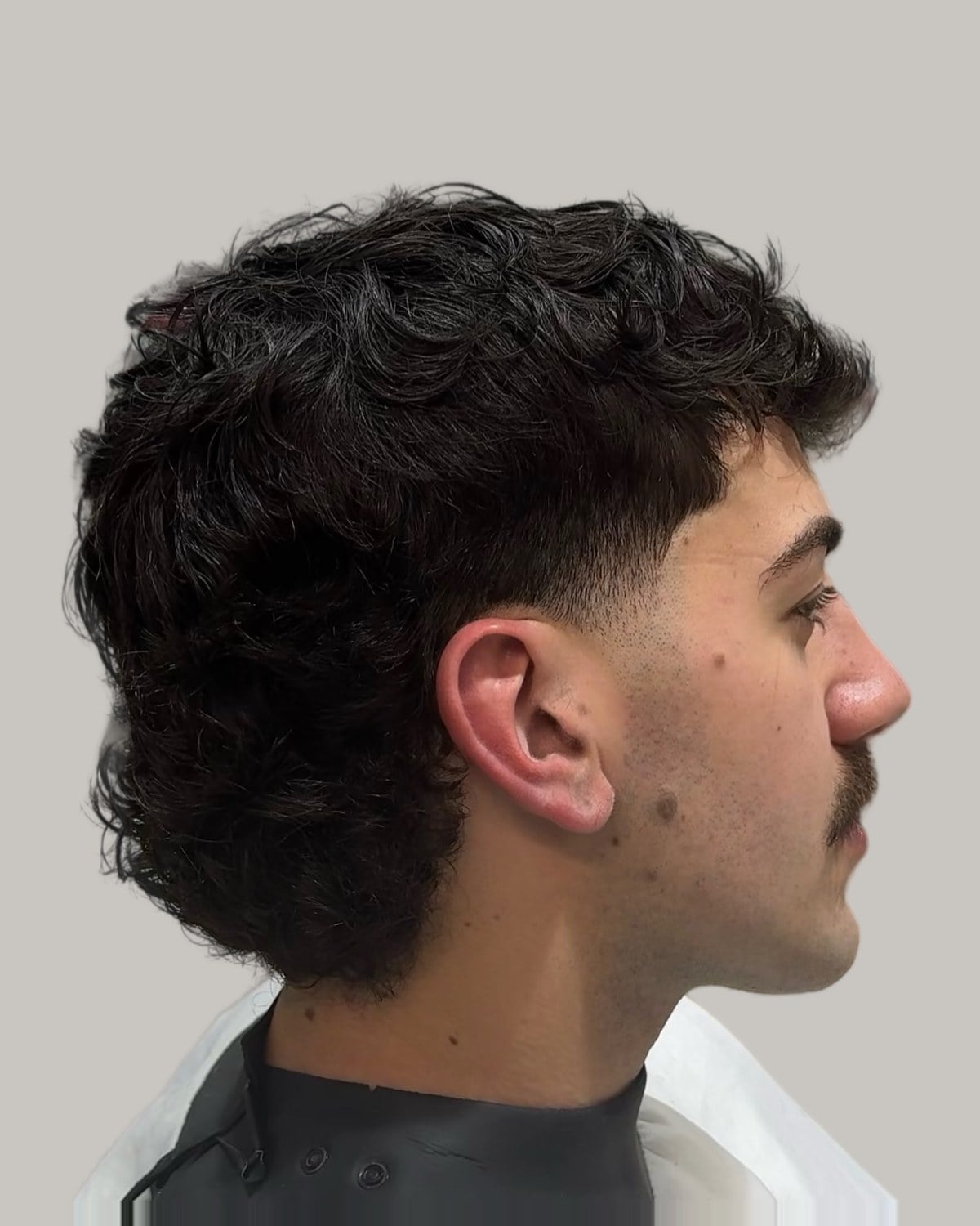 Man with a mustache and a textured dark curly mullet, seen in profile