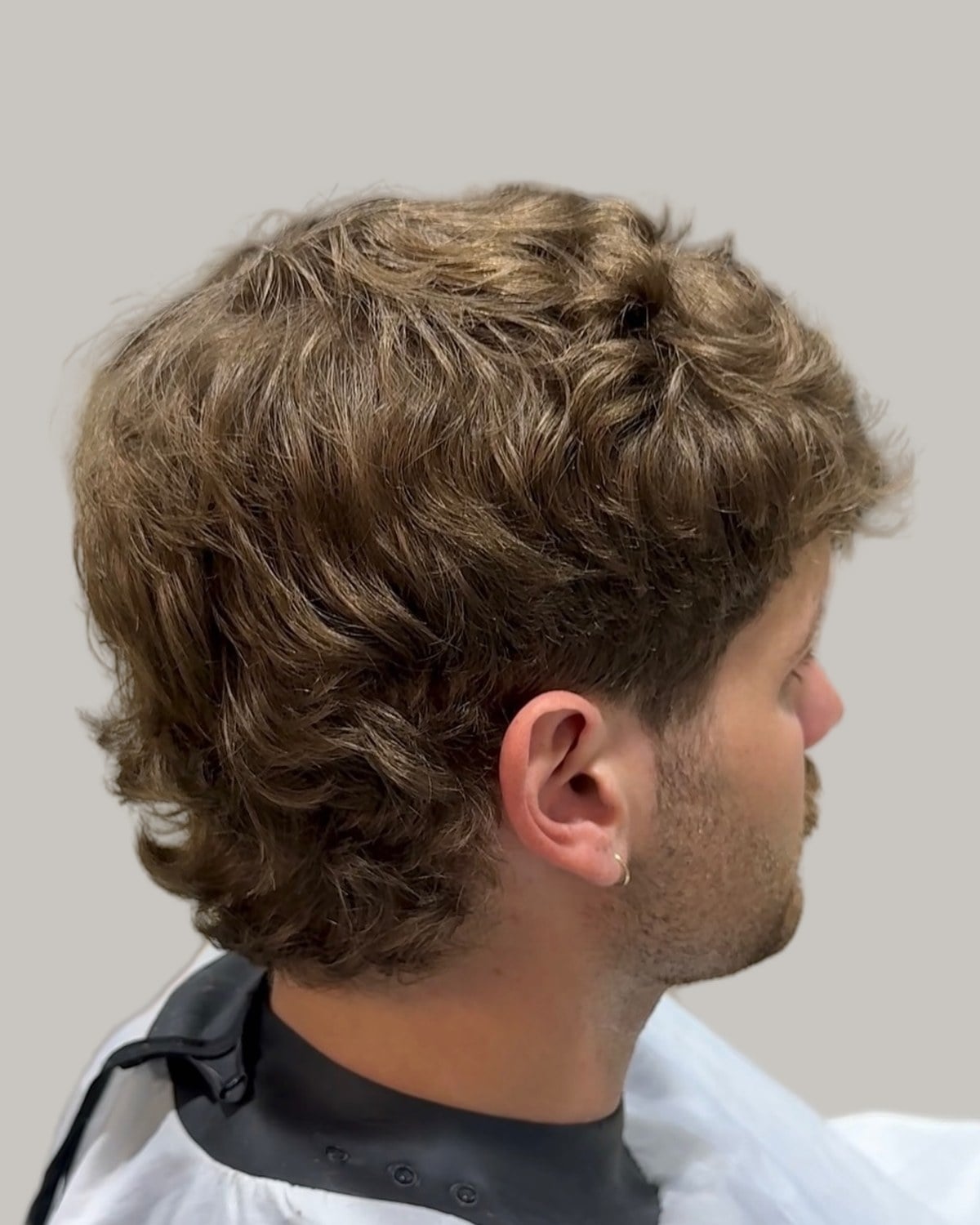 Man with a wavy light brown mullet, seen from behind at an angle