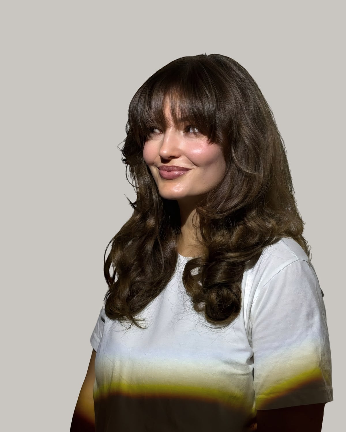 Woman in a white T-shirt turned to one side, long rounded brunette layers