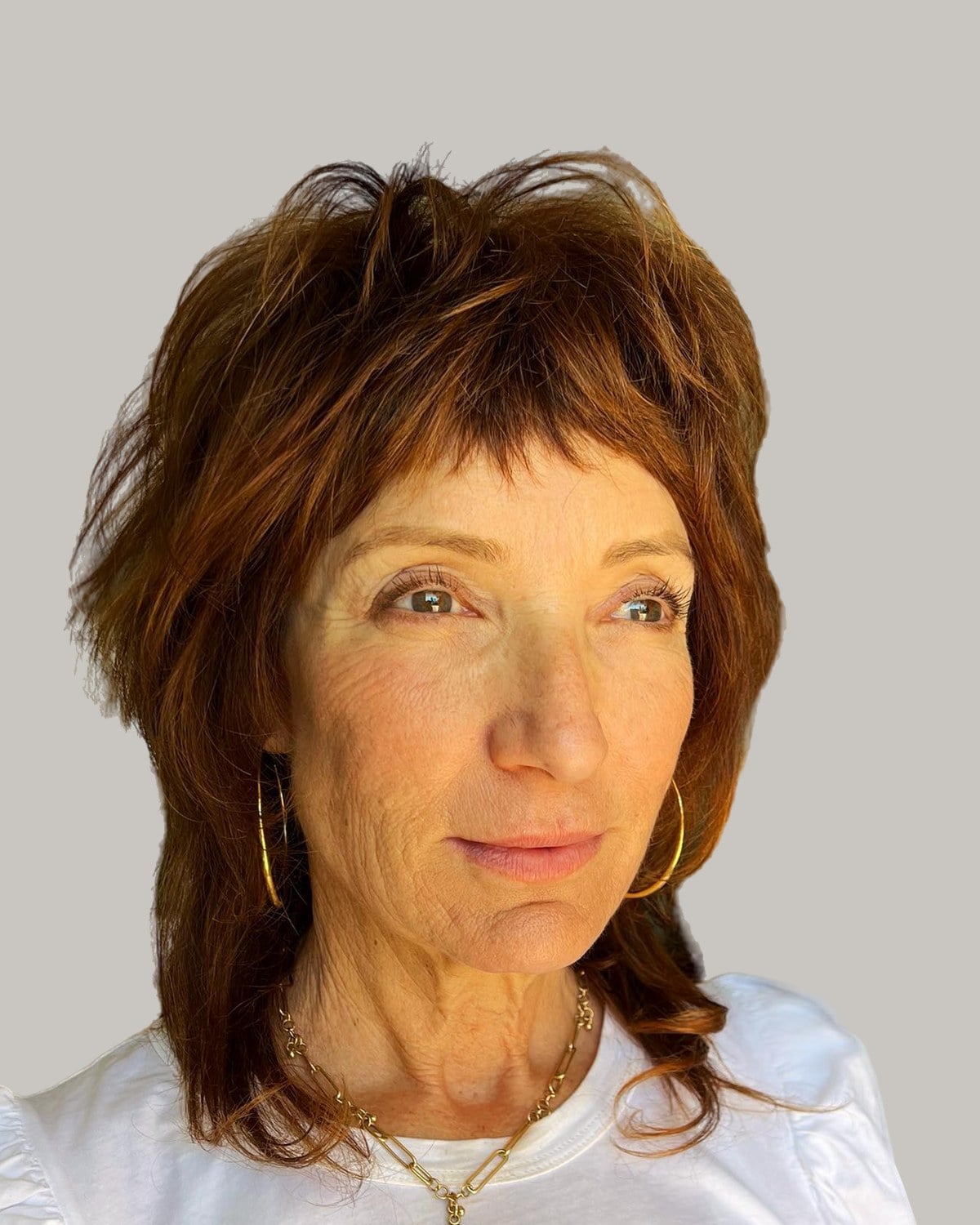 Woman in a white T-shirt facing the camera, auburn shag with short bangs