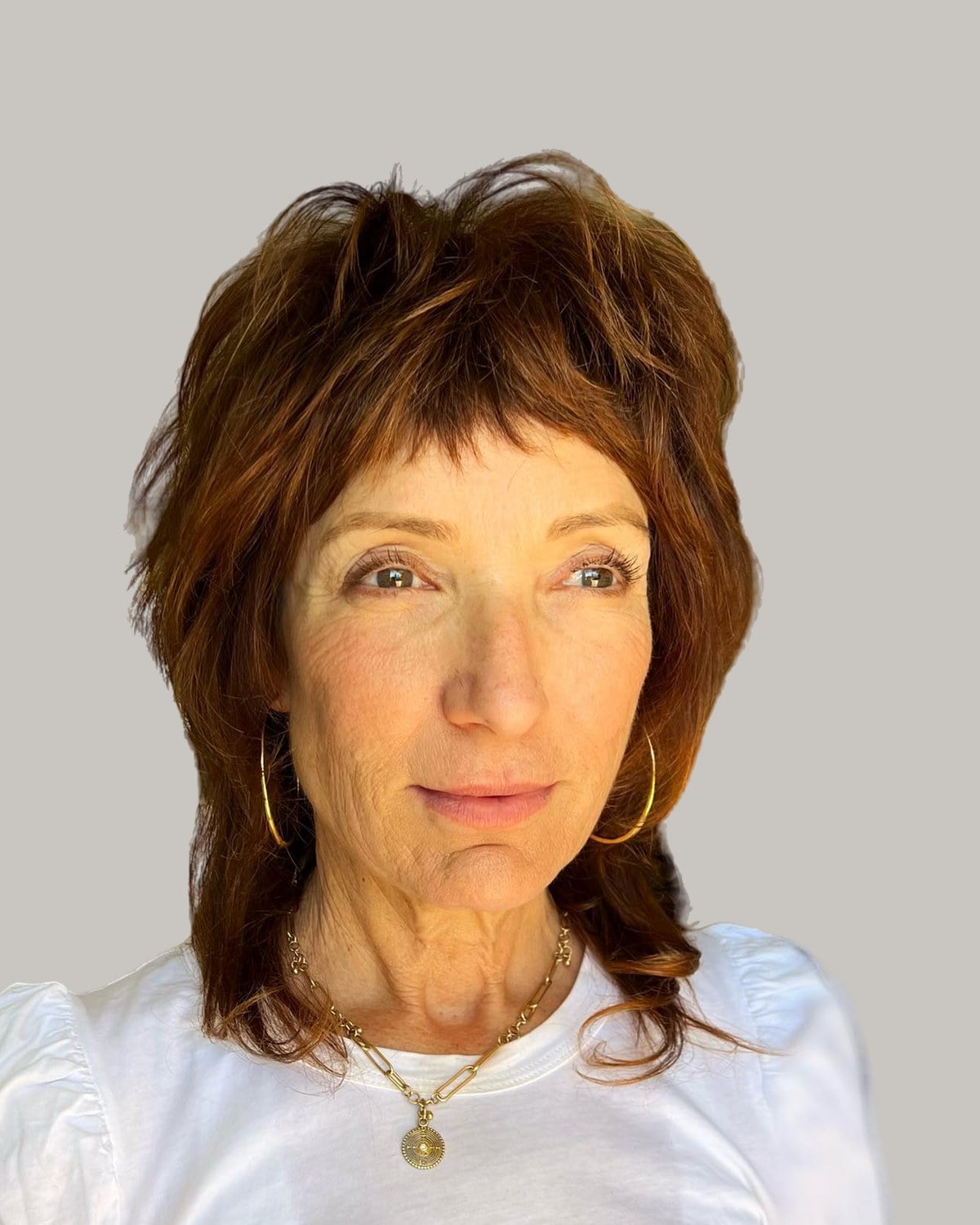 Woman in a white T-shirt and hoop earrings with an auburn shag and micro bangs