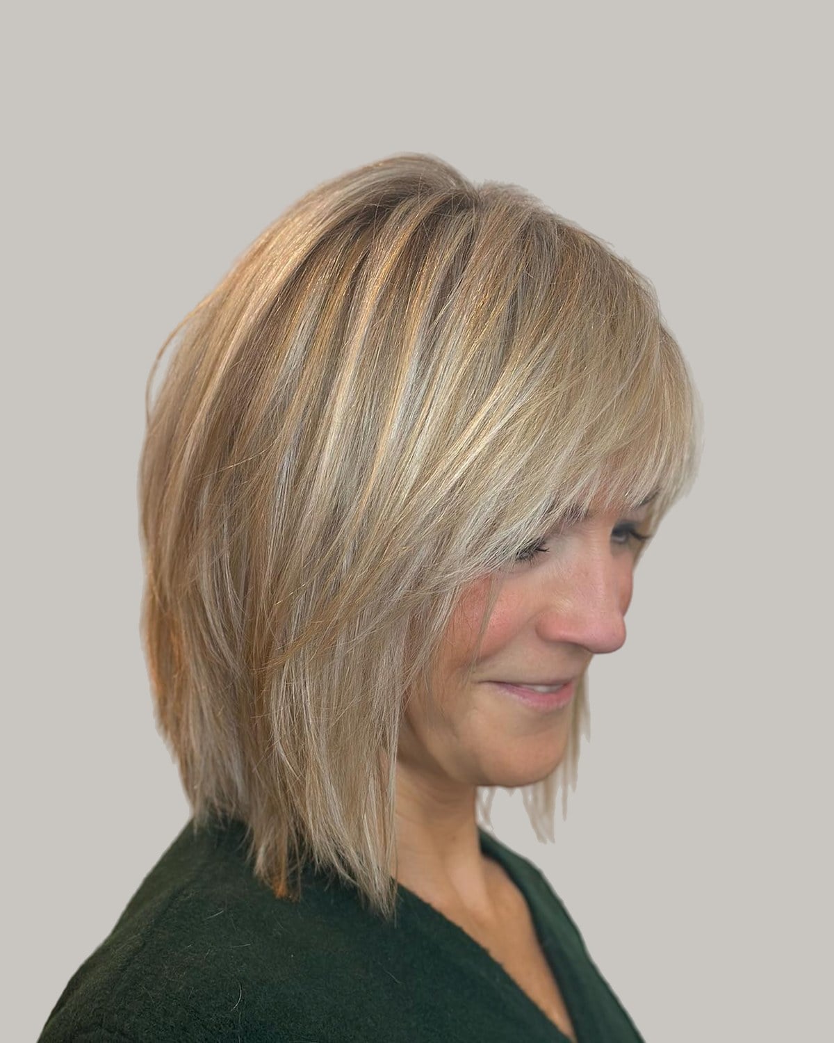 Smiling woman in a green top seen in profile, blonde layered shag with side-swept bangs