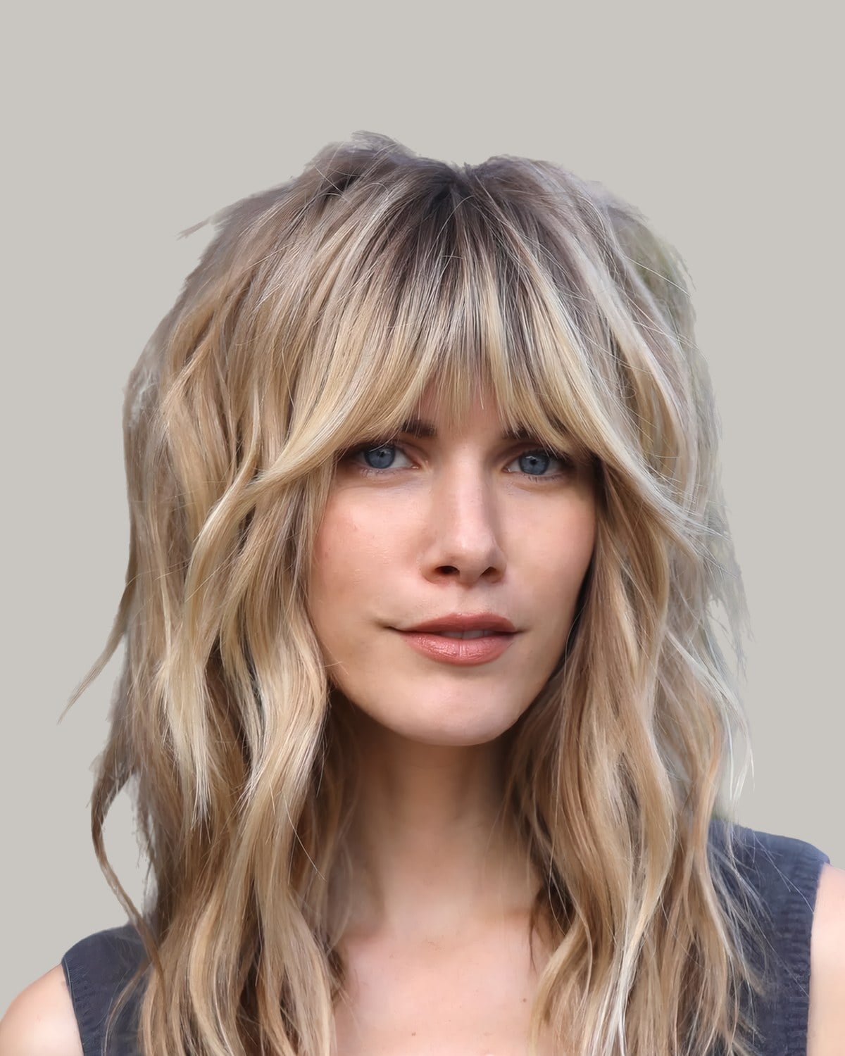 Woman with long blonde waves, a darker root and wispy curtain bangs