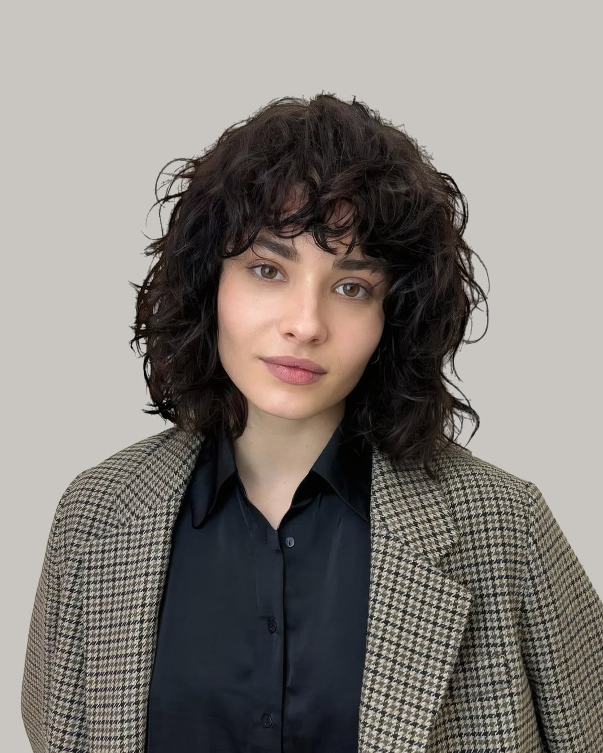 Woman in a houndstooth blazer with a jaw-length dark curly shag and curly bangs