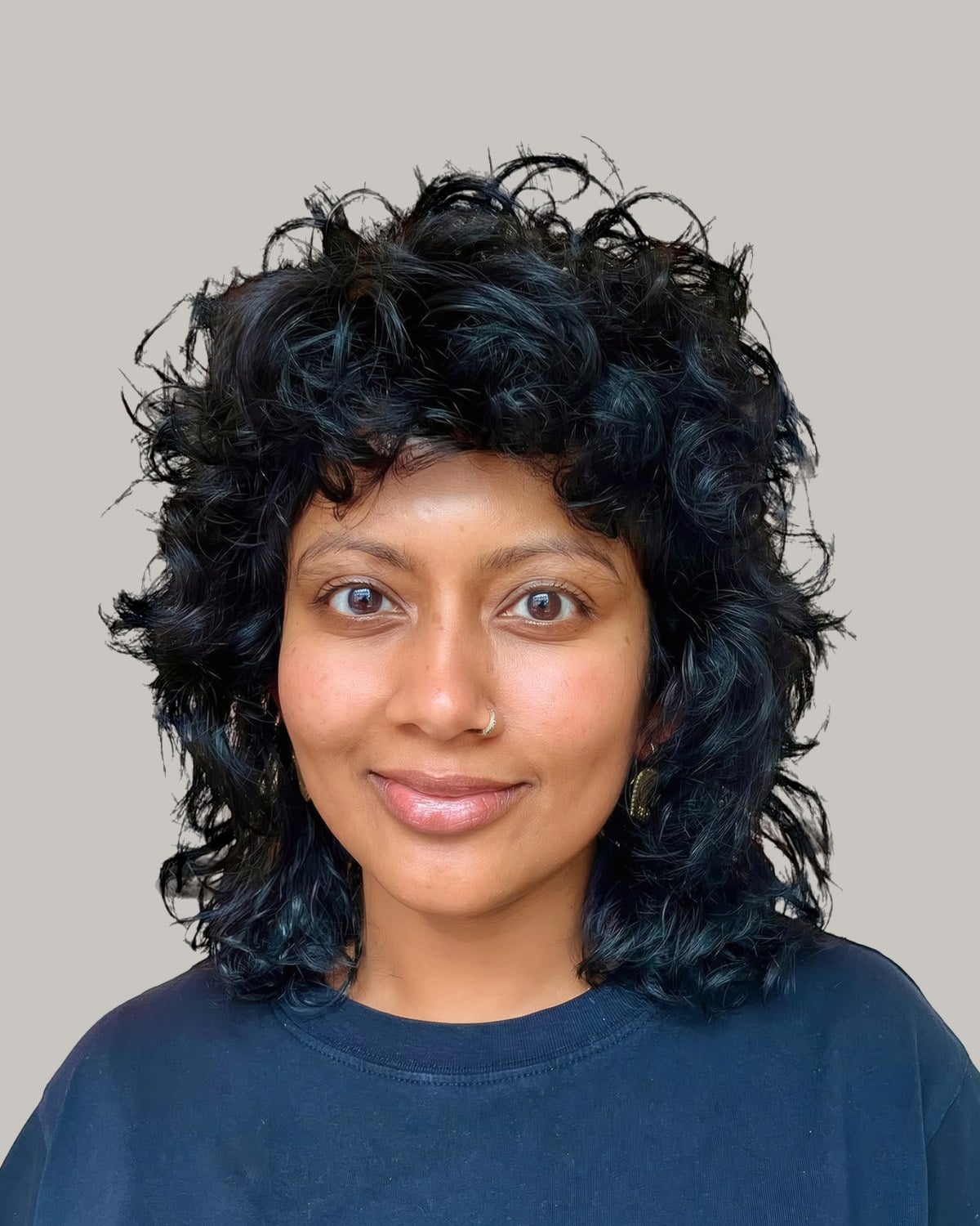 Woman in a navy T-shirt with a blue-black curly shag and curly bangs