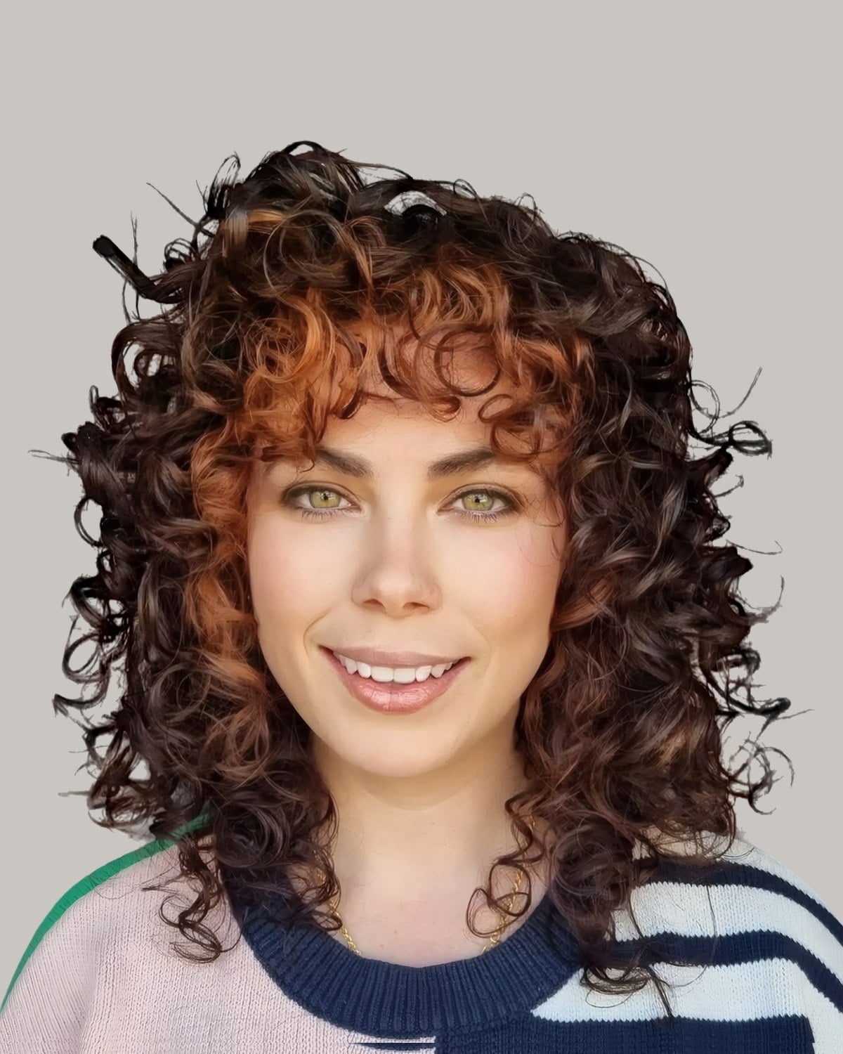 Smiling woman in a striped sweater with copper-tipped brown curls and curly bangs