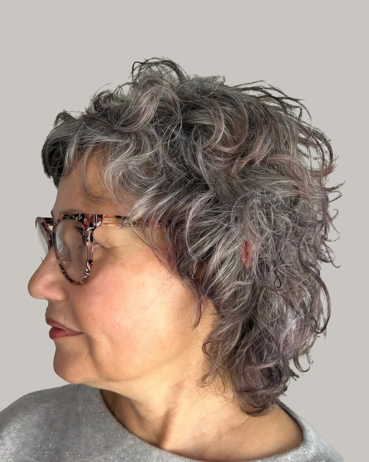 Woman in tortoiseshell glasses and a gray sweater seen in profile, jaw-length silver curls