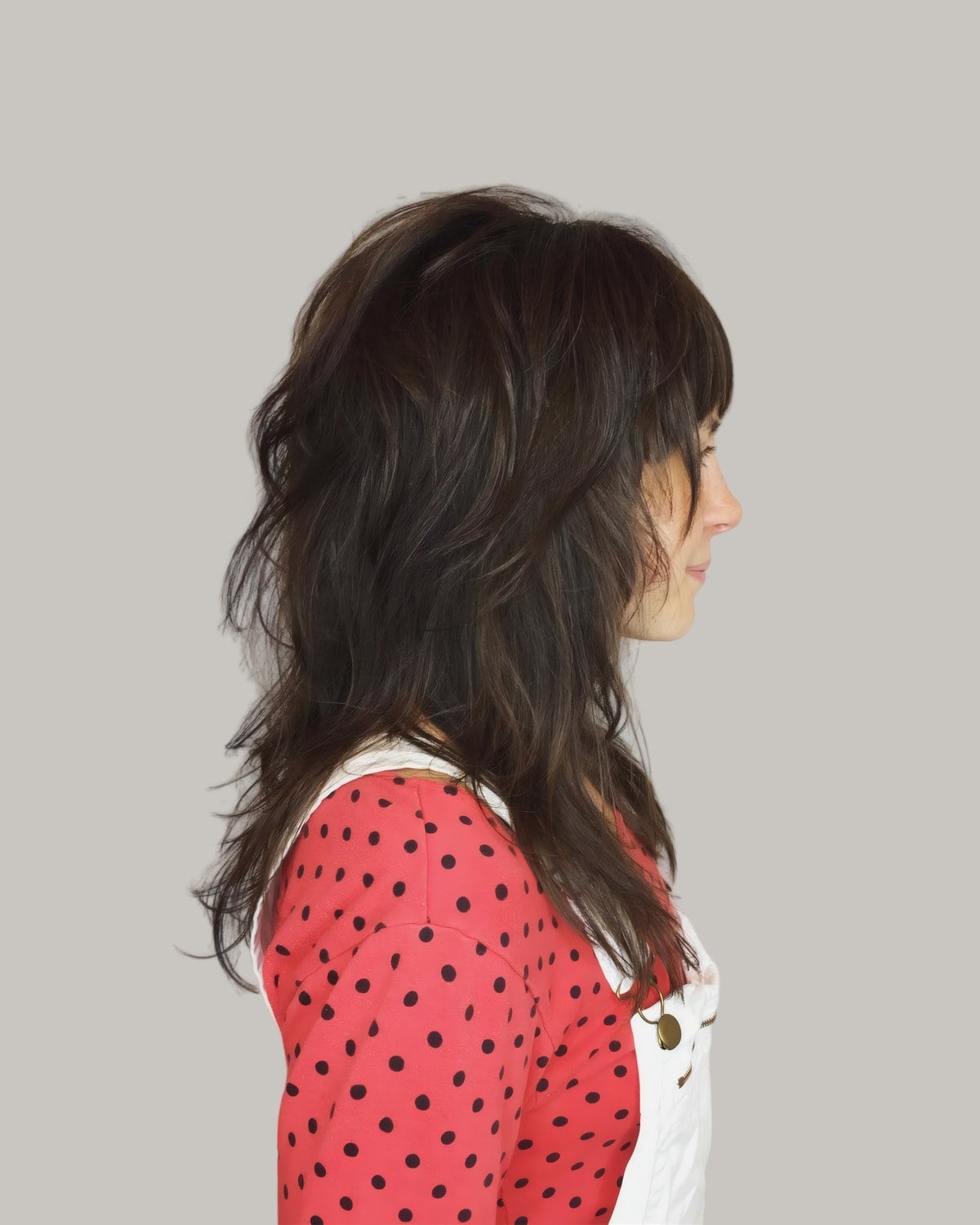 Woman in a red polka-dot top seen in profile, long dark brown shag with bangs