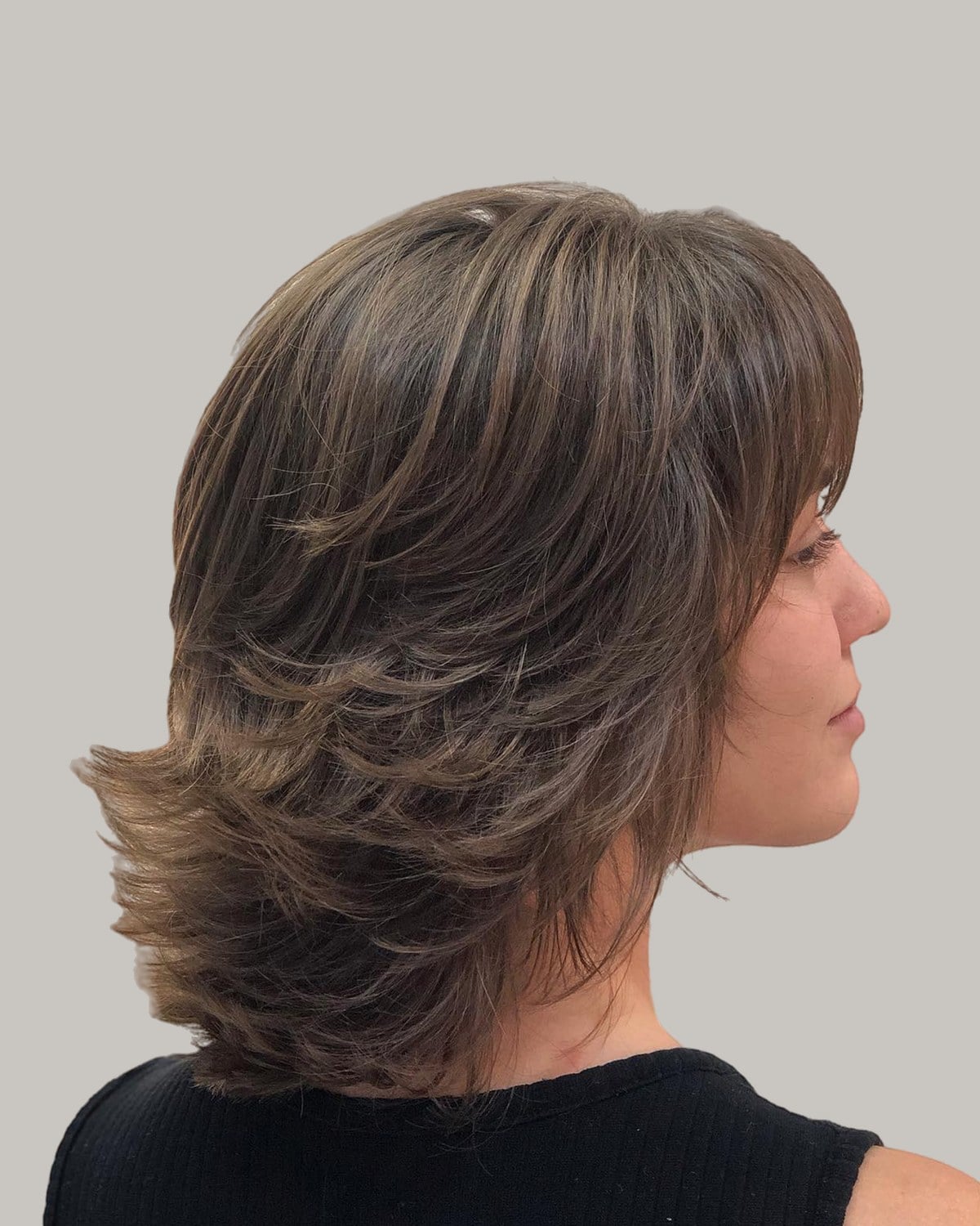 Woman in a black top seen in profile, medium brunette shag with bangs and flicked ends