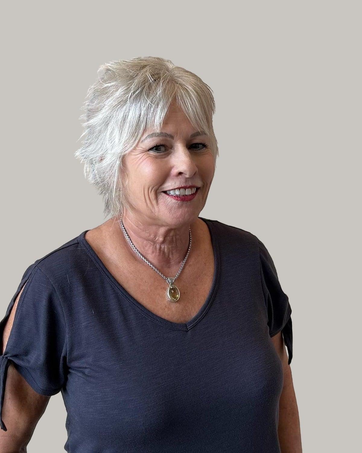 Smiling woman in a navy T-shirt with a short platinum shag and choppy bangs
