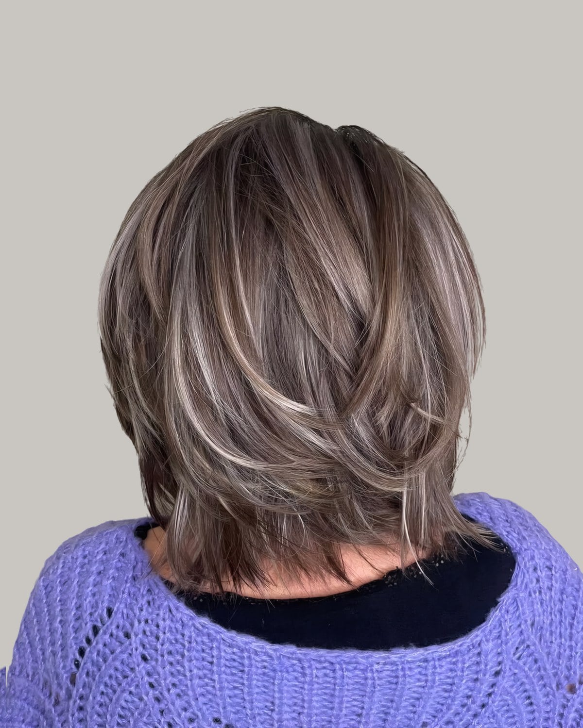Back view of a chin-length shaggy bob, brown with silver highlights, over a purple sweater
