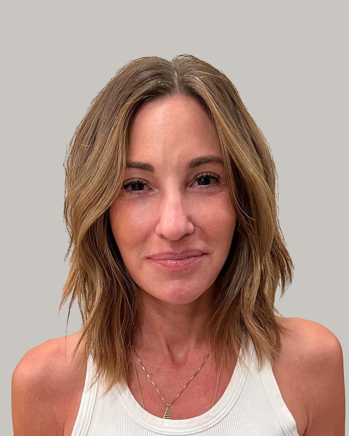 Woman in a white tank top with a brown shaggy lob, highlights and a center part