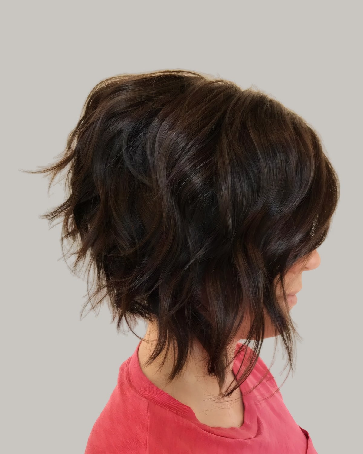 Dark brown, choppy shaggy bob seen from behind and to one side, over a red T-shirt