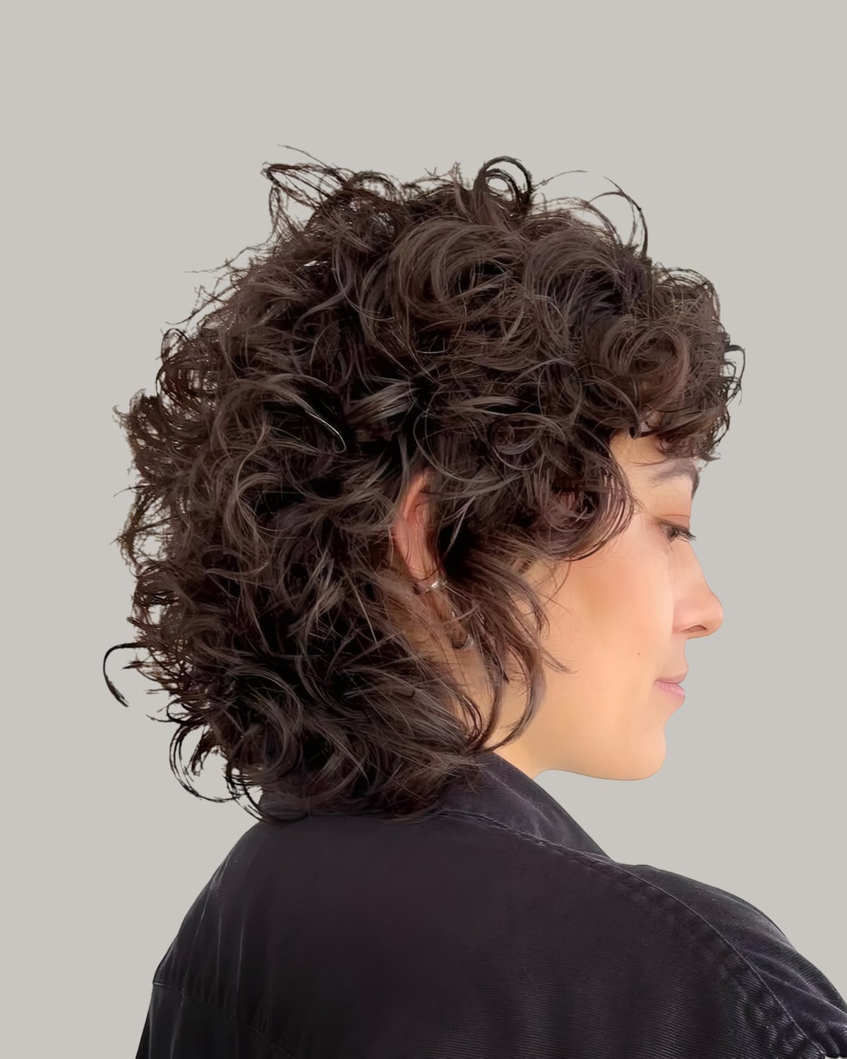 Woman in a dark top seen in profile, short curly shag piled at the crown
