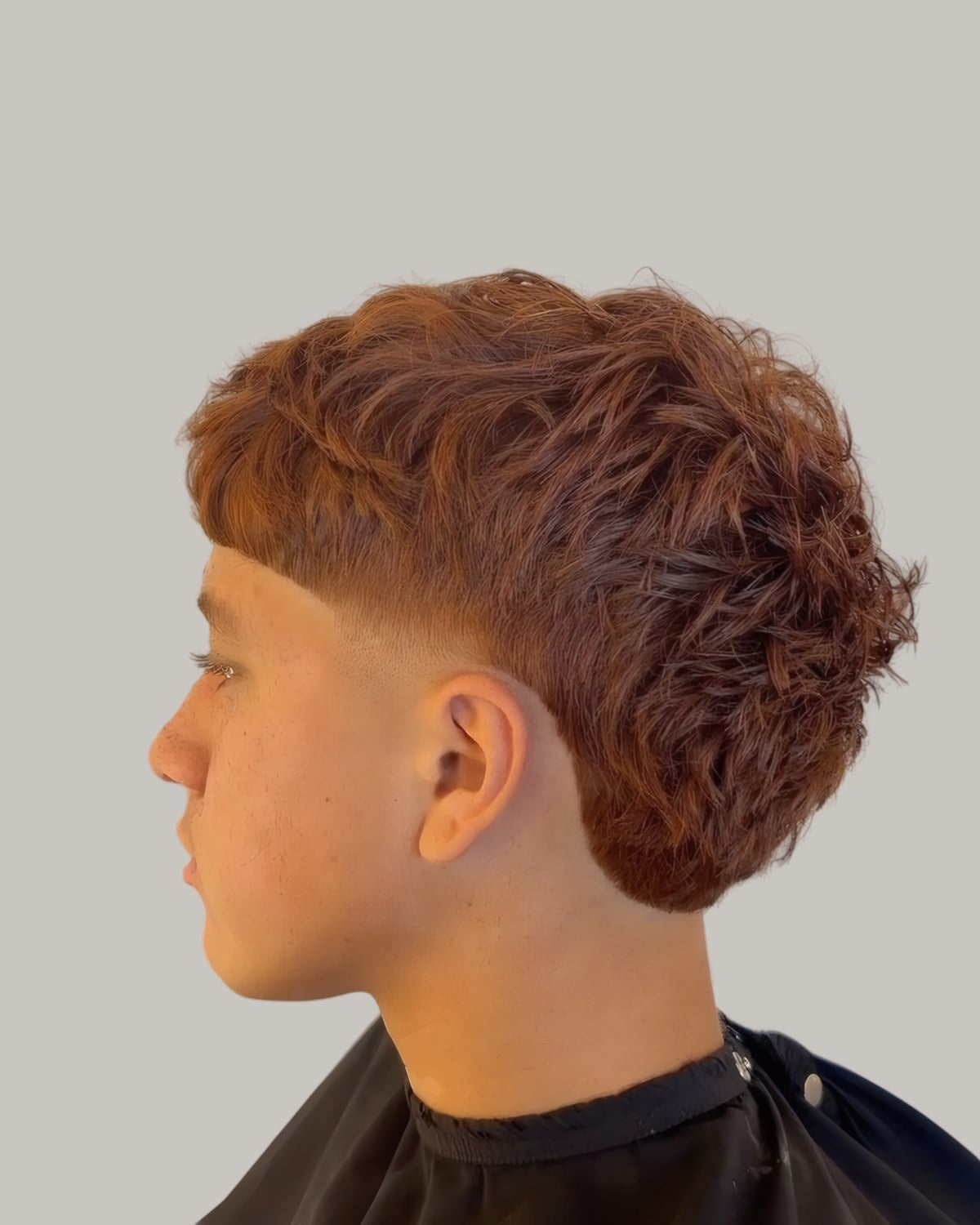 Young man with copper-dyed curls and a low fade, seen in profile
