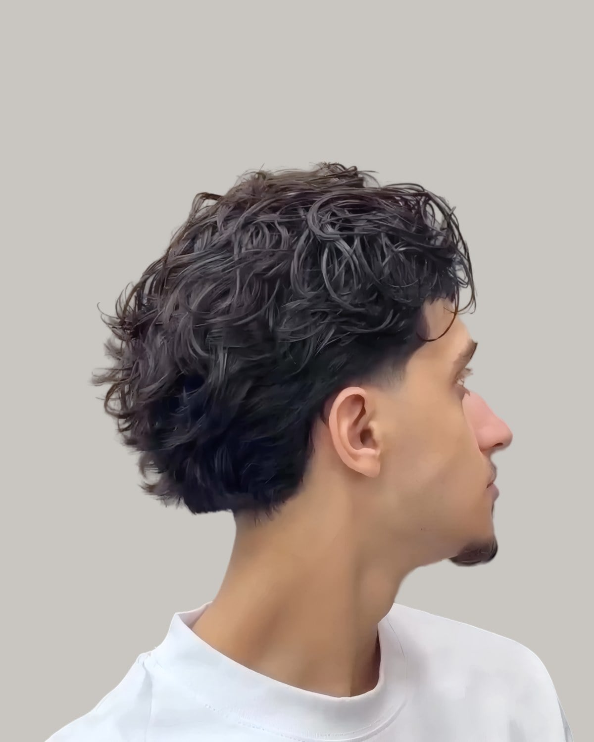 Young man with loose curls and a low taper, seen in profile
