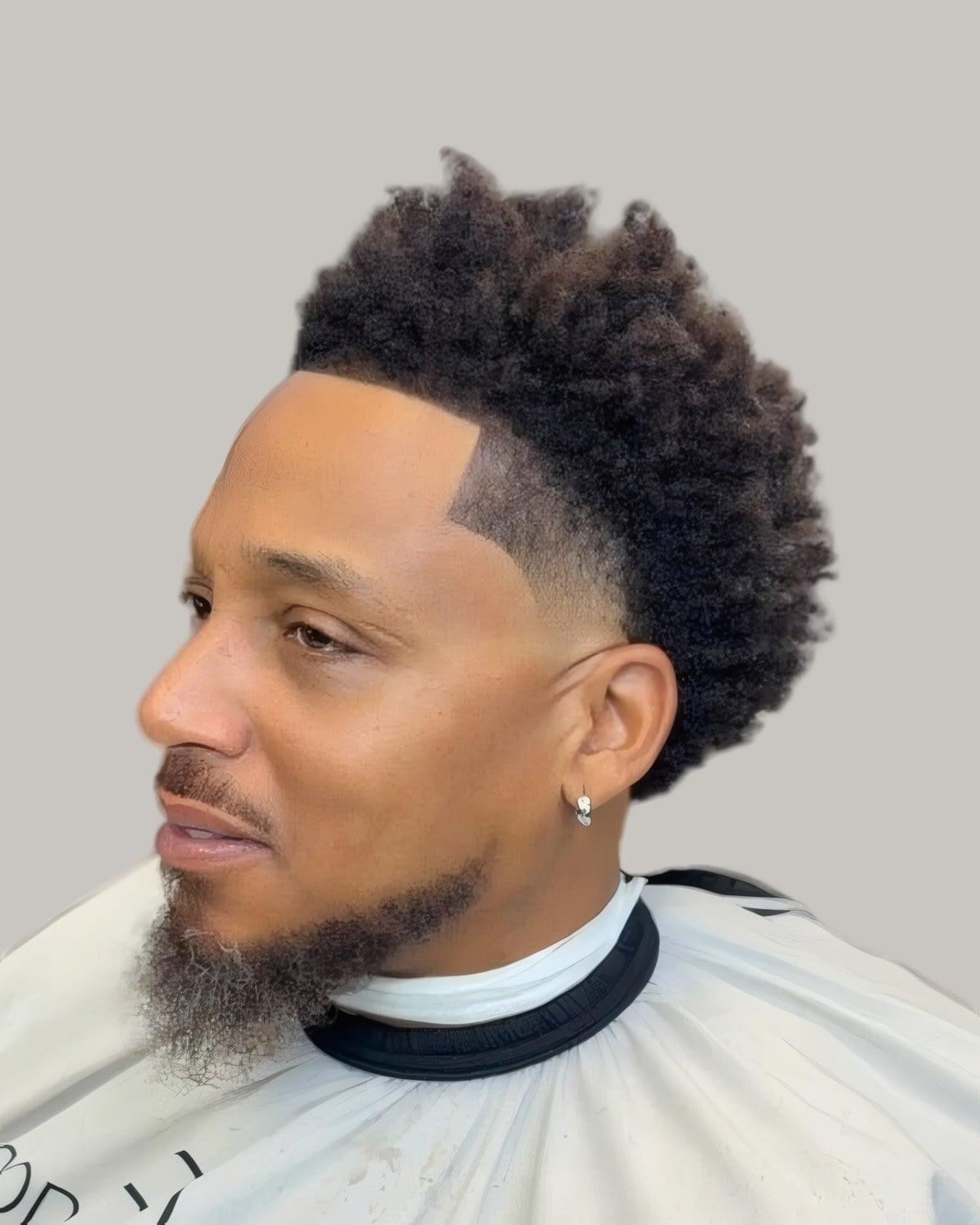 Bearded Black man with a curly top and a high taper, seen in profile