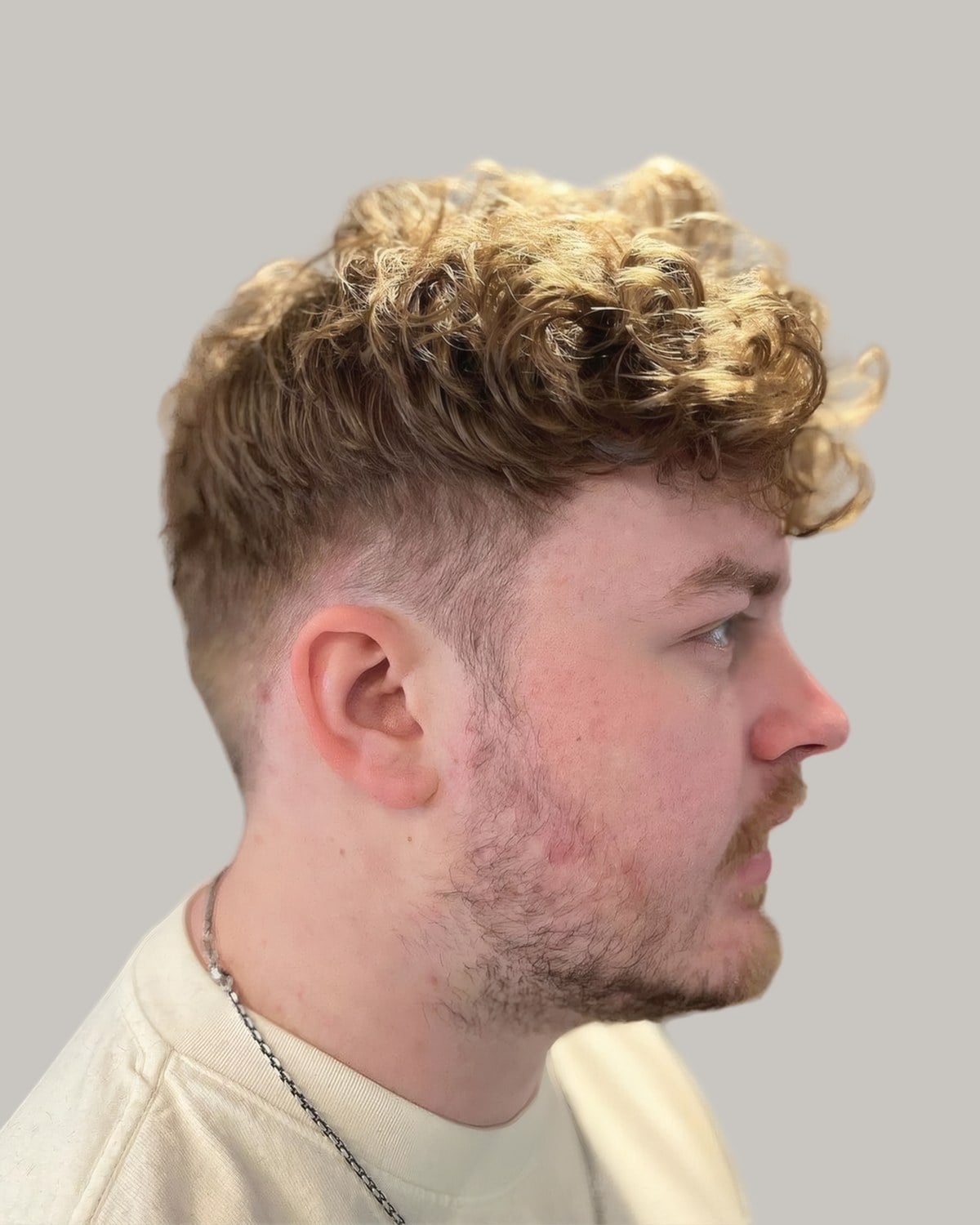 Bearded man with a curly blond blowout and a mid taper, seen in profile