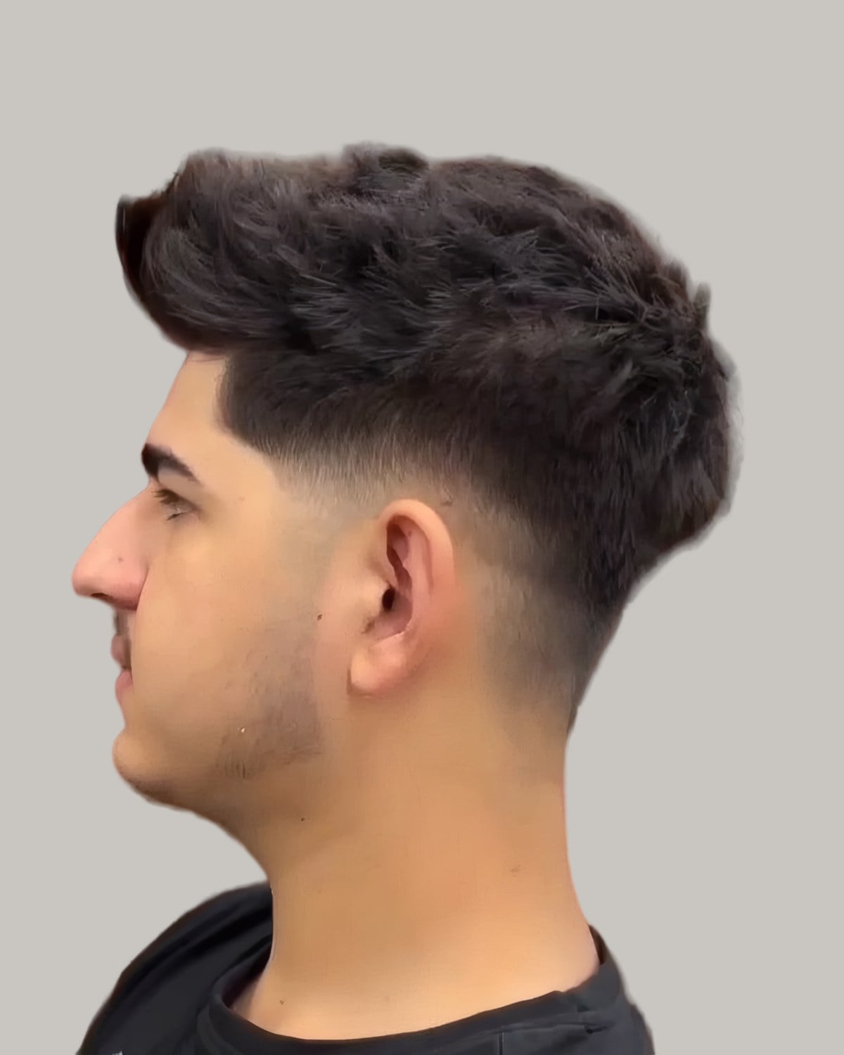 Man with a thick textured top and a mid fade, seen in profile