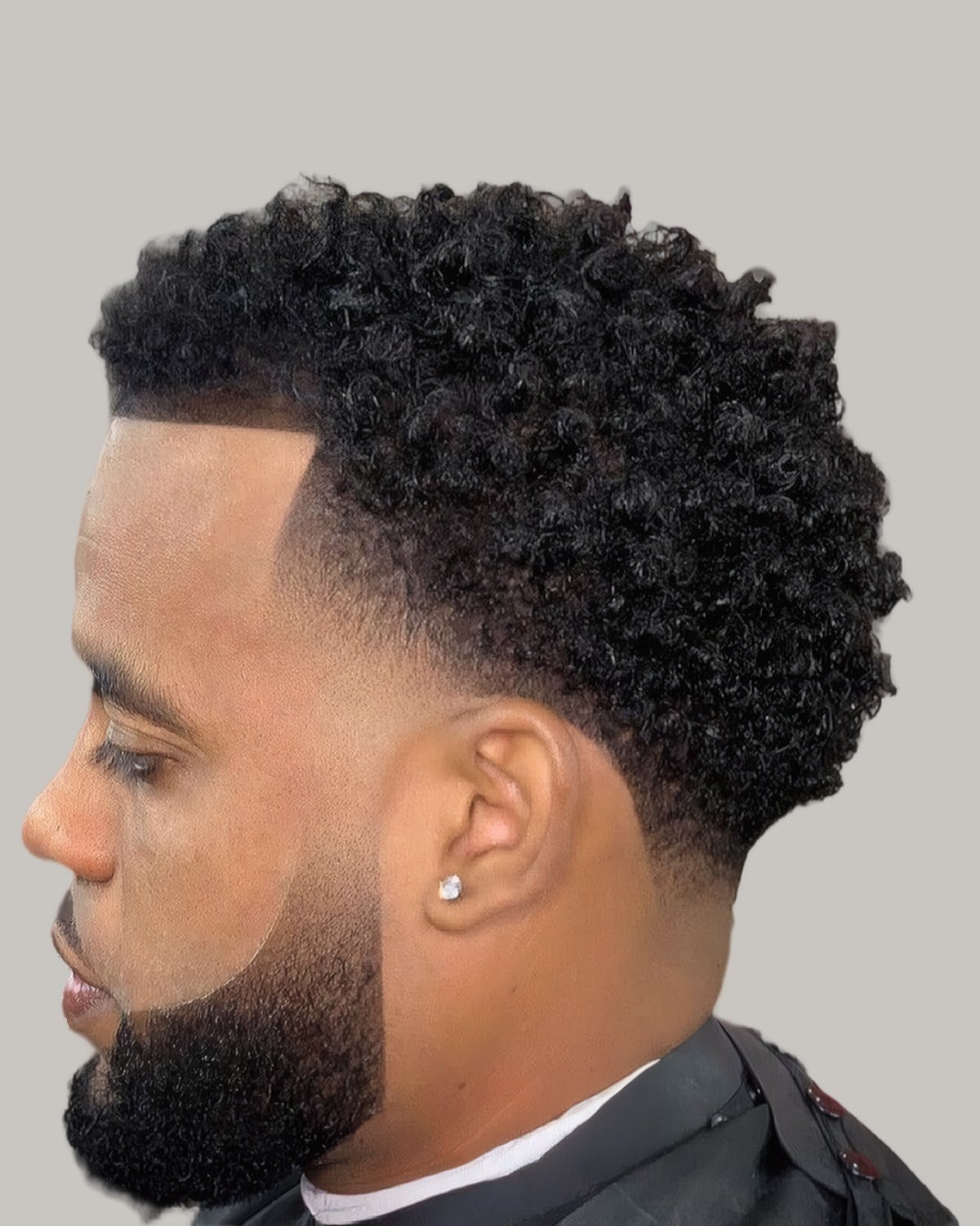 Bearded Black man with a curly top and a mid taper, seen in profile