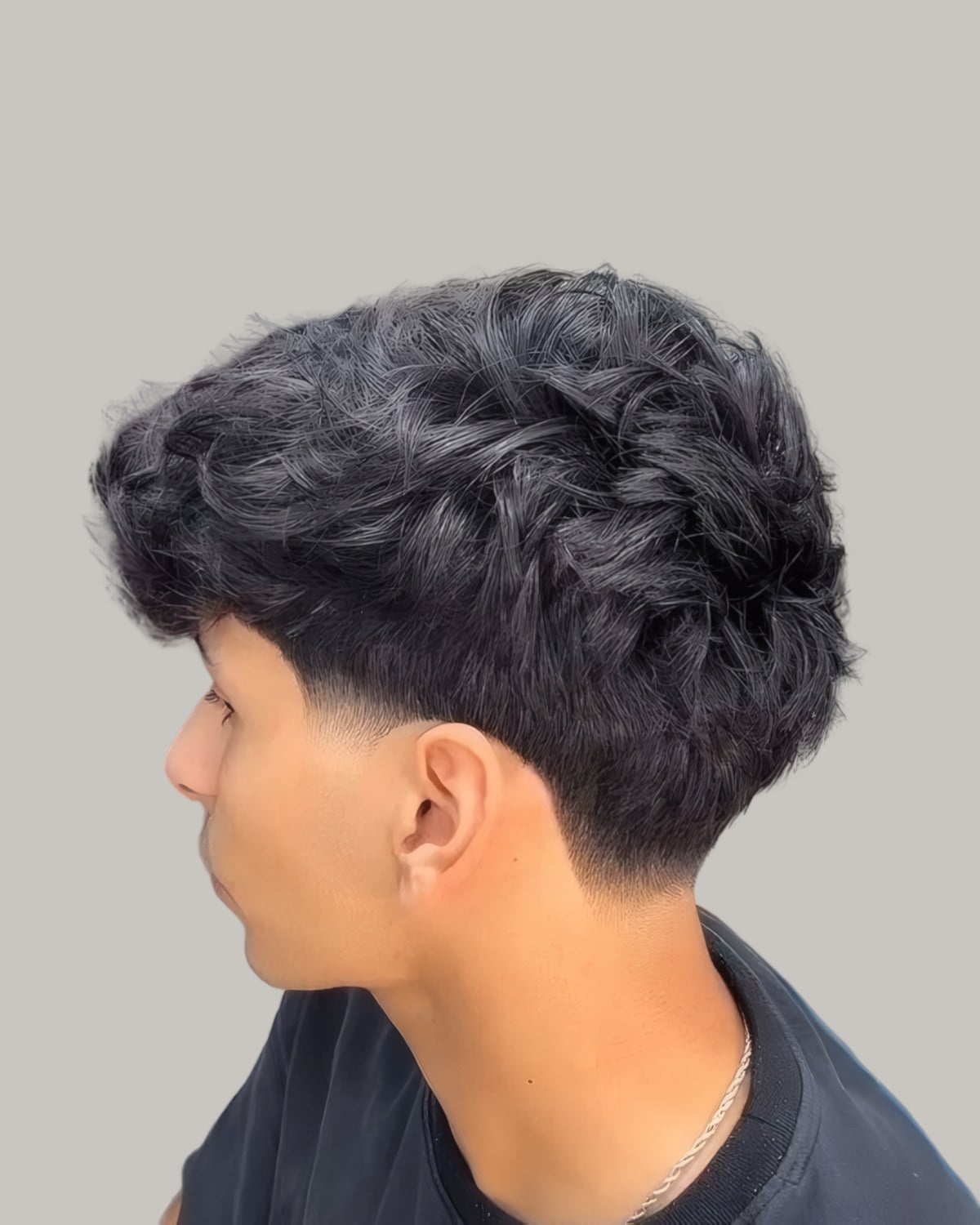 Young man with a wavy top and a low taper, seen in profile