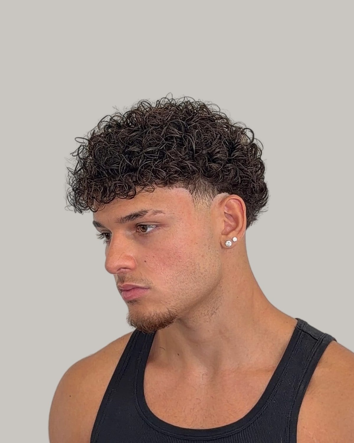 Young man with a curly top and a low taper, seen in profile