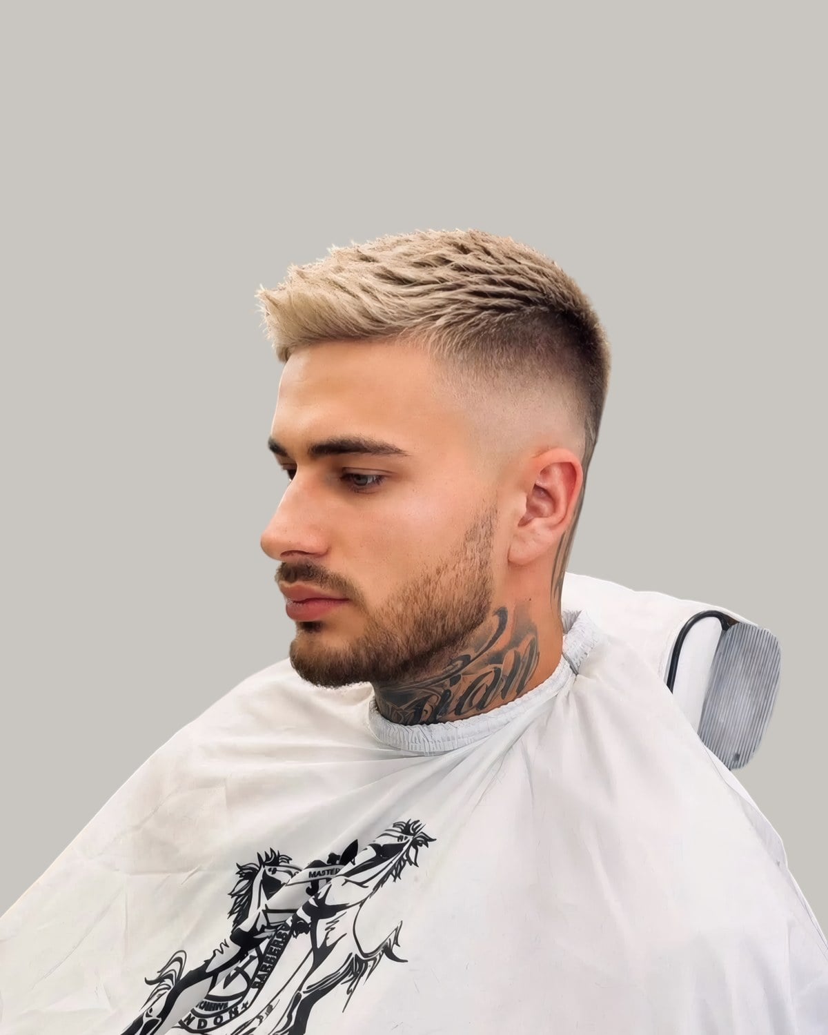 Man with a bleached textured crop, a high skin fade and a beard, in a barber's cape