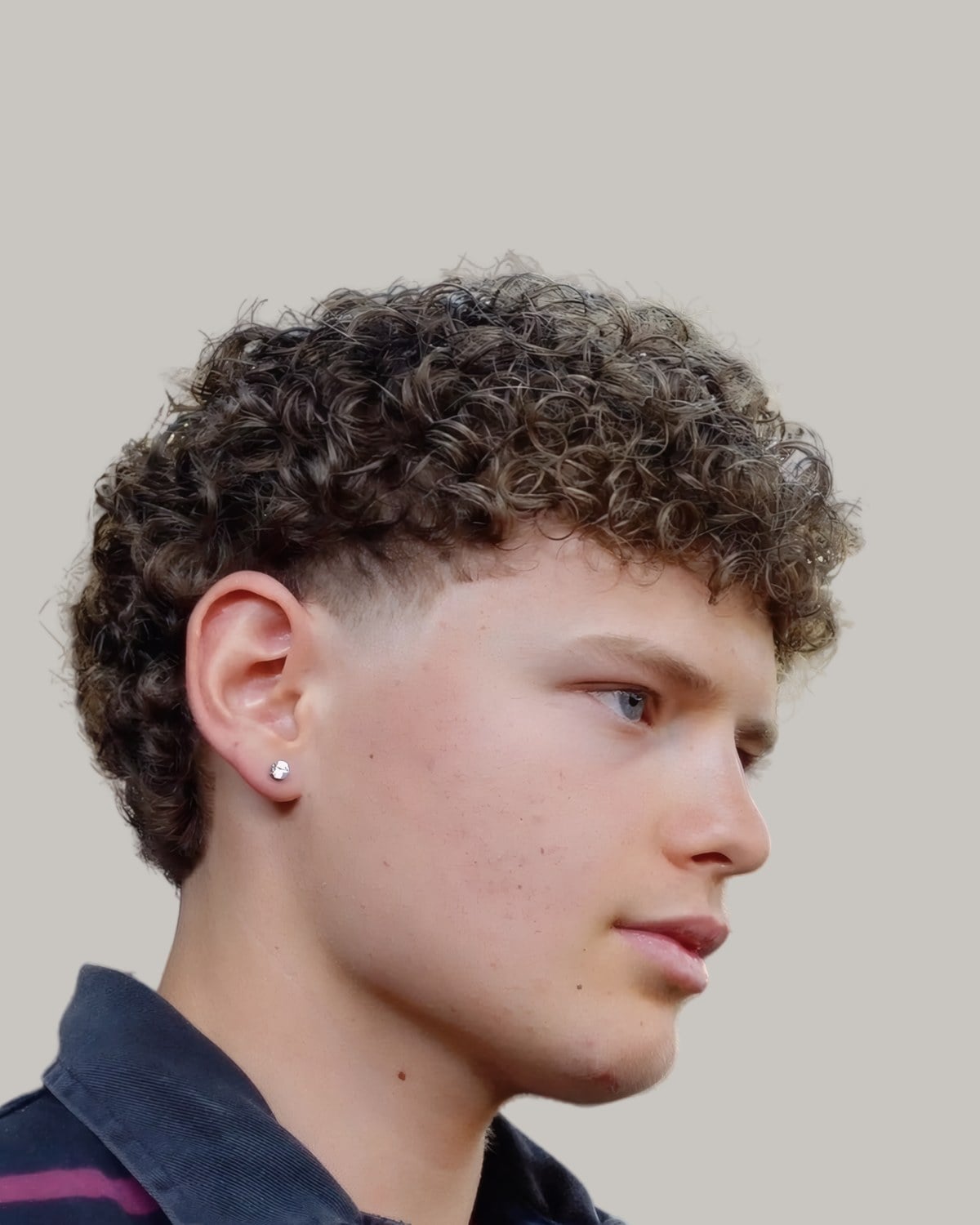 Young man with a curly textured crop and a burst fade, looking to the side