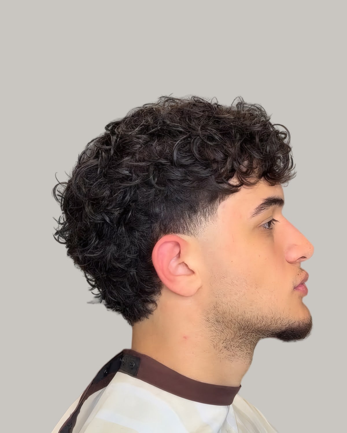 Man with a longer curly textured crop and a taper, seen in profile