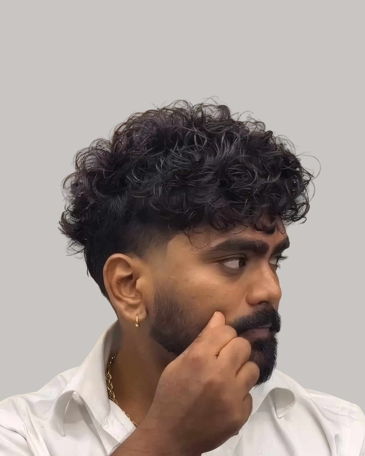Man with a curly textured crop and a full beard, hand on his chin