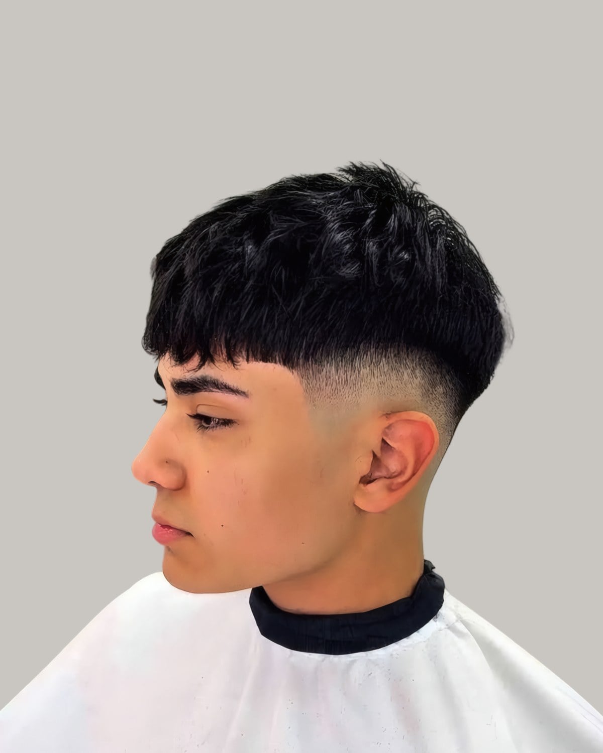 Young man with a black French crop and a fade, in a white barber's cape