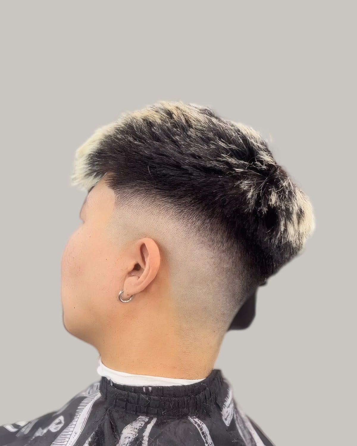 Man with a dark textured crop with bleached tips and a skin fade, seen from behind