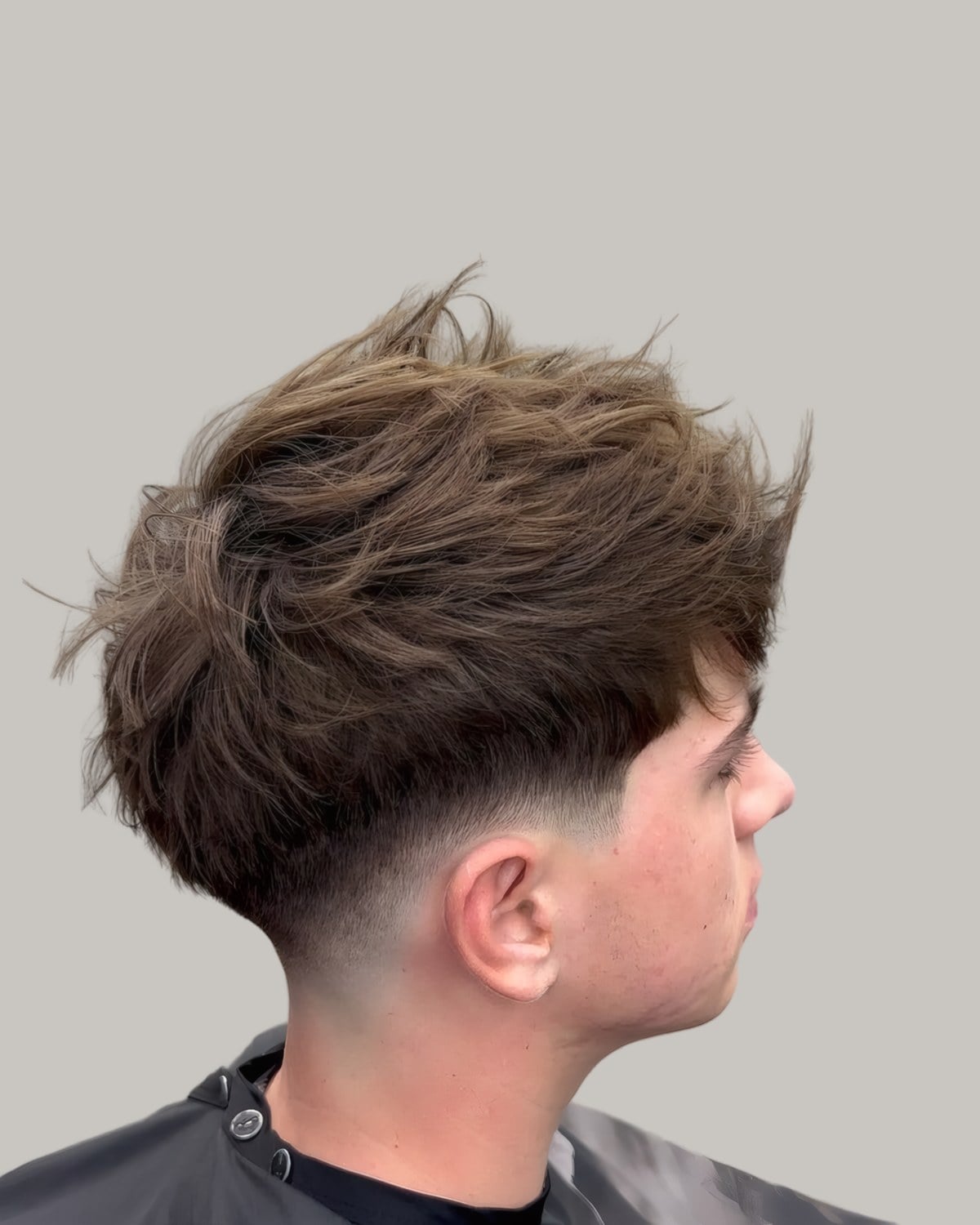Man with a long, messy textured crop and a low fade, seen from the side