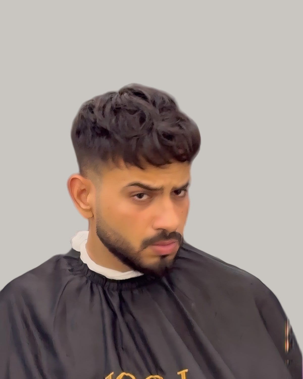 Man with a wavy textured crop, a mid fade and a short beard, in a barber's cape