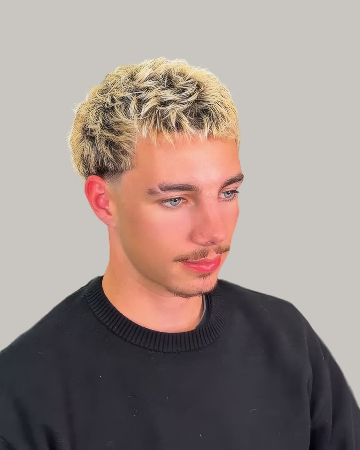 Young man with a bleached textured fringe and a mustache, facing the camera