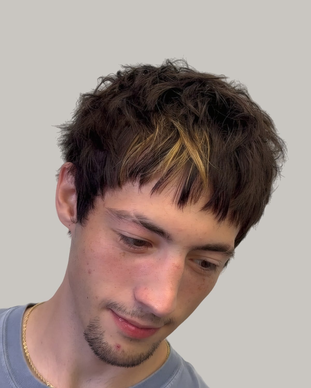 Young man with a dark textured fringe with blond streaks, looking down