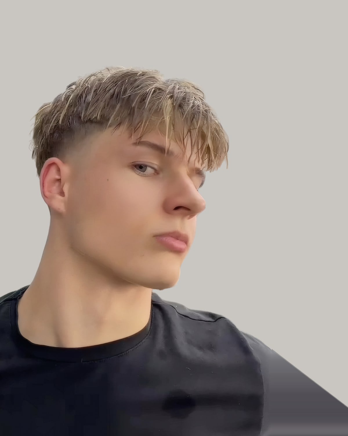 Young man with a blond textured fringe and a taper, looking to the side
