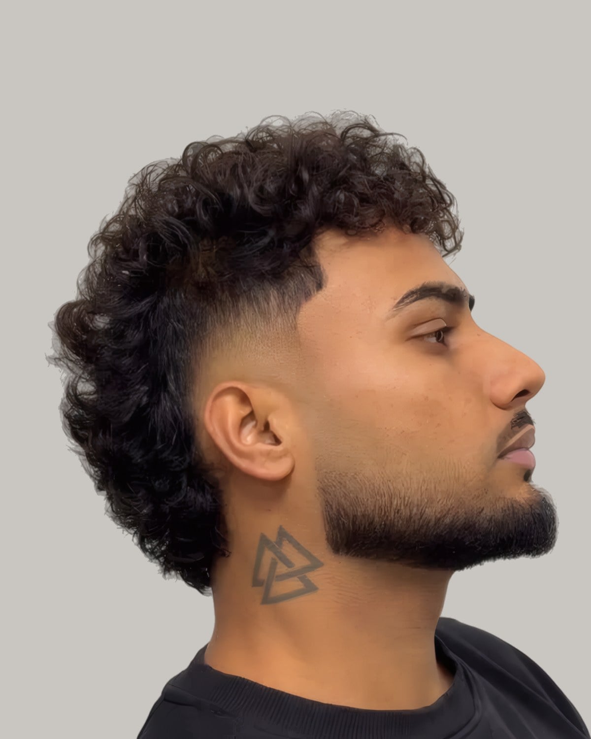 Bearded man with a curly top and a high taper, seen in profile