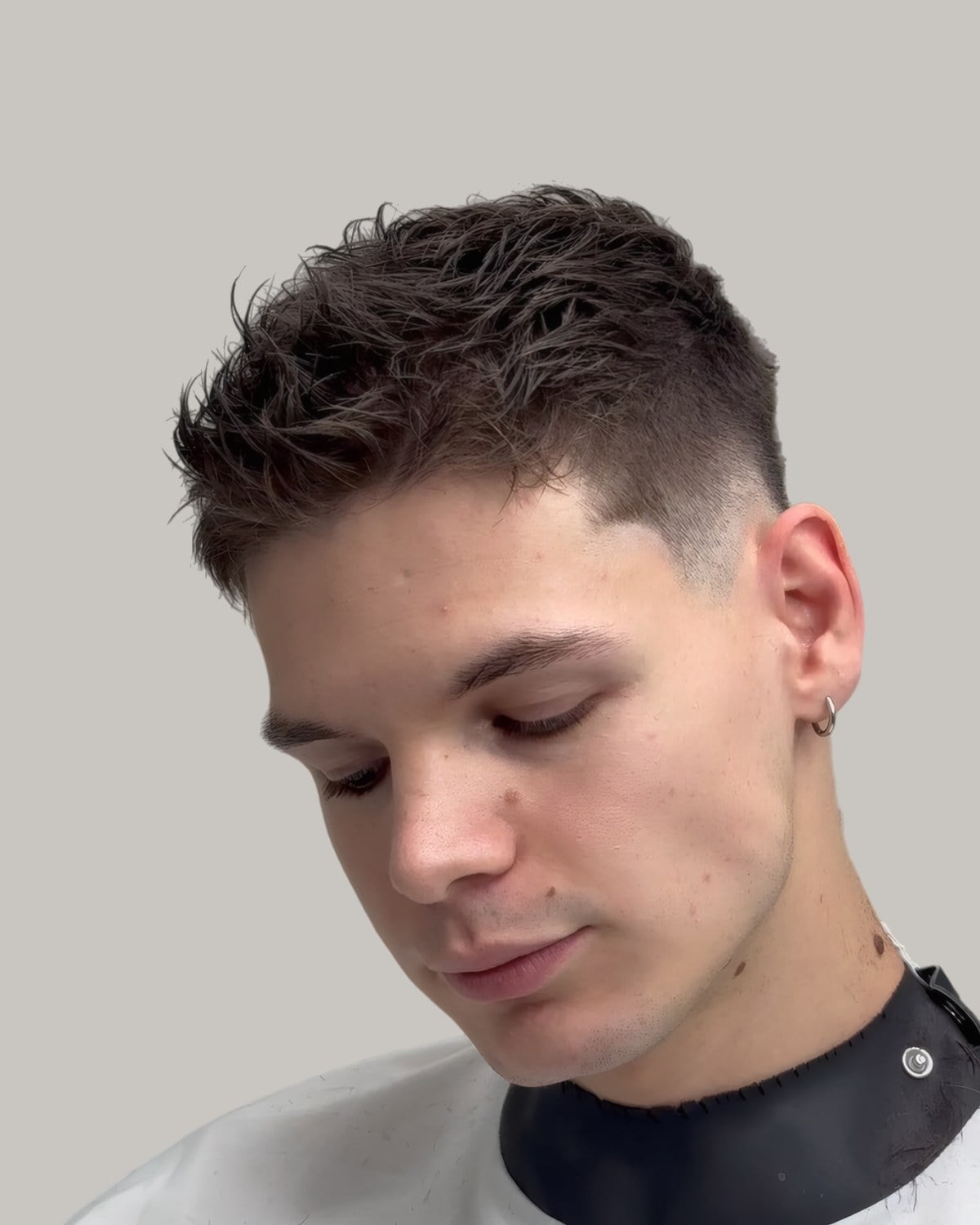Young man with a short textured fringe and a low taper, looking down to one side