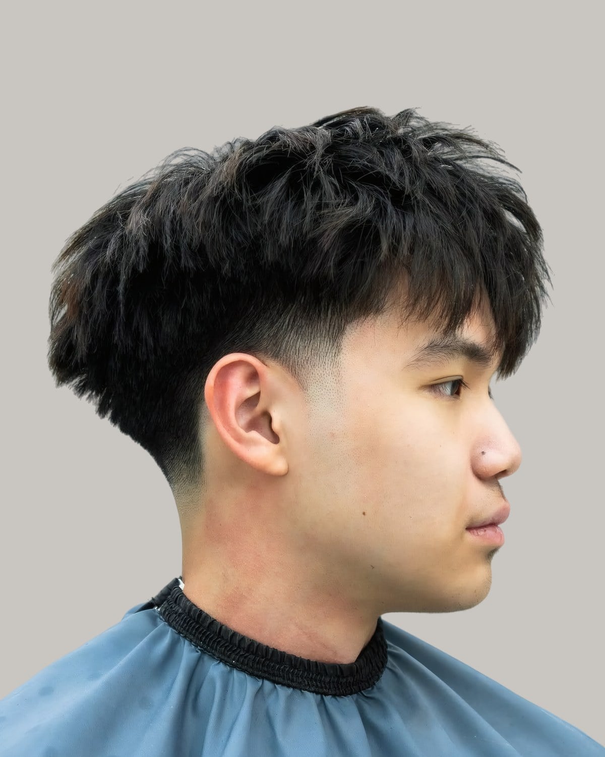 Young Asian man with a heavy textured fringe and a fade, seen from the side