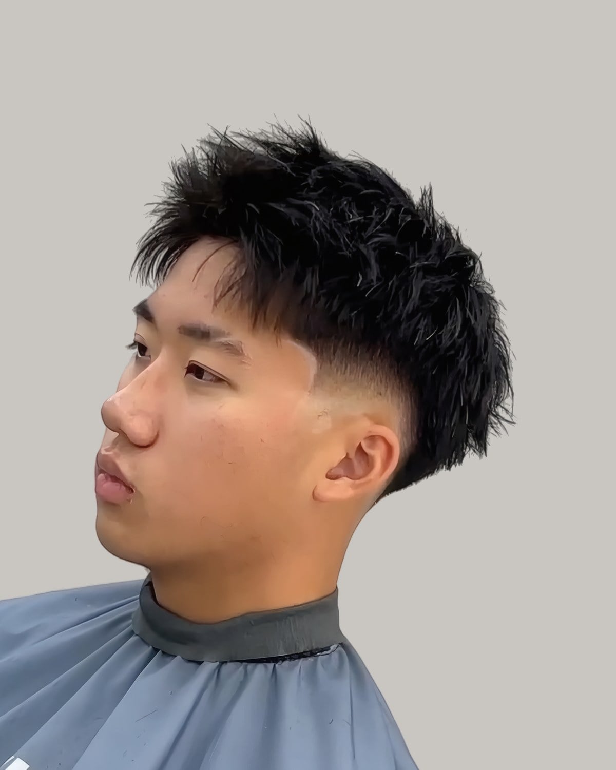 Young Asian man with a spiky textured fringe and a mid fade, seen at an angle